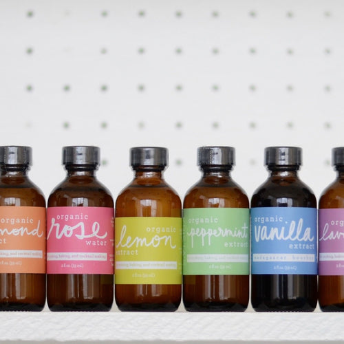 6 glass bottles with pastel colored labels filled with flavor extracts
